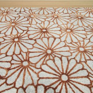 Gray textured rug with a repeating raised rust-brown daisy pattern on a pale wooden floor.