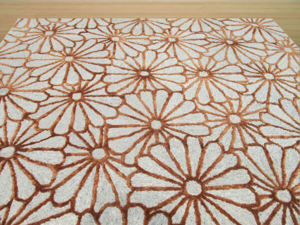 Gray textured rug with a repeating raised rust-brown daisy pattern on a pale wooden floor.