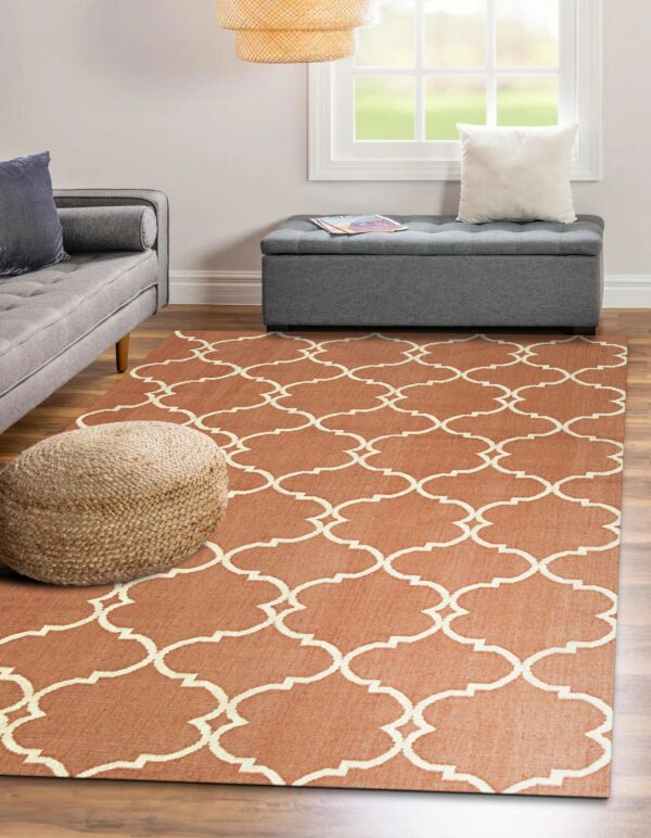 A rust orange flatweave rug with a cream quatrefoil pattern sits on wood floors near gray furniture.