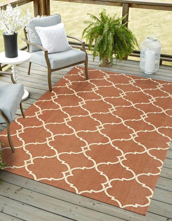 A terracotta rug with a cream quatrefoil lattice pattern sits on a gray wood deck with patio chairs and plants.