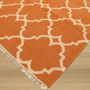 Orange and cream low-pile rug with a geometric trellis pattern and short fringe on light wood flooring.