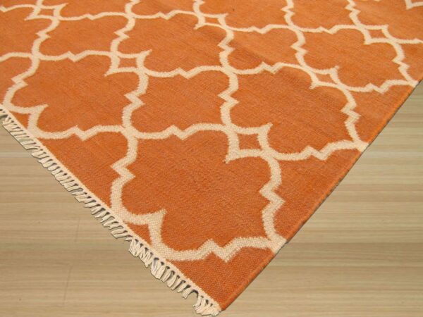 Orange and cream low-pile rug with a geometric trellis pattern and short fringe on light wood flooring.