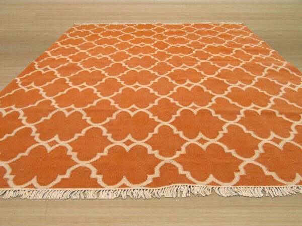 Orange and cream low-pile rug with a repeating ogee pattern and fringe on light wood flooring.