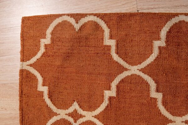 Textured, burnt orange rug with a bold cream trellis pattern sits on light wood flooring.