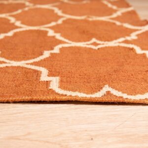 Low-angle view of a flat woven orange and cream rug featuring a trellis pattern on blonde wood planks.