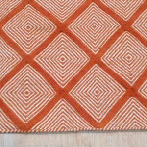 A textured orange and white rug featuring a repeating diamond geometric pattern on light wood flooring.