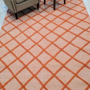 Textured orange and white rug with concentric diamonds placed beneath a beige armchair and dark wooden table legs.