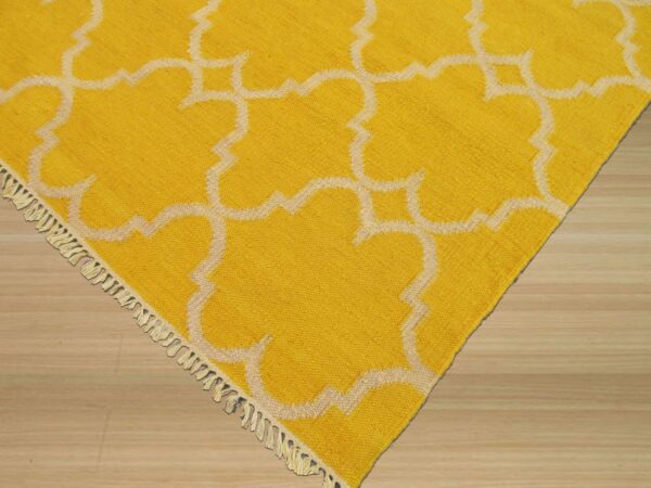 Yellow rug featuring a raised off-white moroccan pattern and tassels shown on light wood flooring.