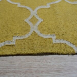 Yellow low-pile rug with a cream geometric quatrefoil pattern rests on light blonde wood flooring.
