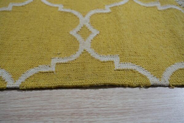 Yellow low-pile rug with a cream geometric quatrefoil pattern rests on light blonde wood flooring.