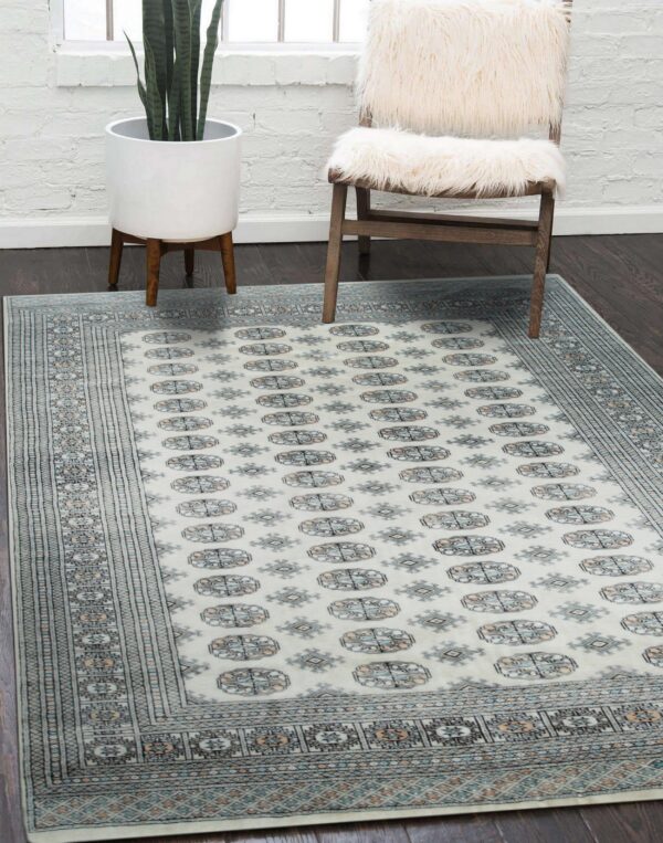 Cream rug with blue and tan geometric medallions lies on dark floor next to a white furry chair.