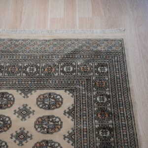 Beige low-pile rug with geometric patterns in black, light blue, and peach on light blonde wood flooring.