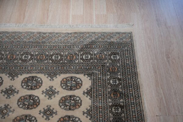 Beige low-pile rug with geometric patterns in black, light blue, and peach on light blonde wood flooring.