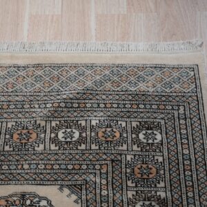 Rug corner showing nested geometric borders in cream, black, peach, and pale blue over wood planks.
