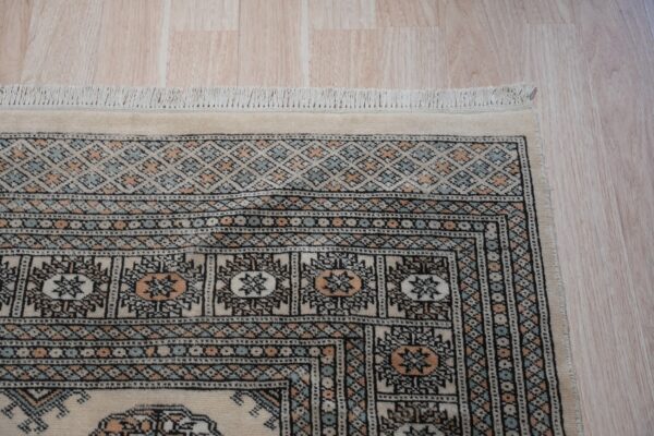 Rug corner showing nested geometric borders in cream, black, peach, and pale blue over wood planks.