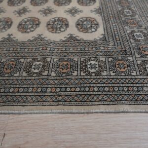 Close-up of a cream rug border featuring intricate black, light blue, and peach geometric designs on wood flooring.