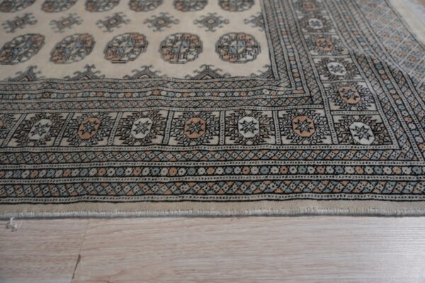 Close-up of a cream rug border featuring intricate black, light blue, and peach geometric designs on wood flooring.
