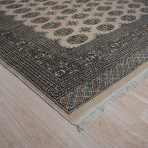 Low pile cream rug featuring geometric guls and a multi-color patterned border on light wood flooring.