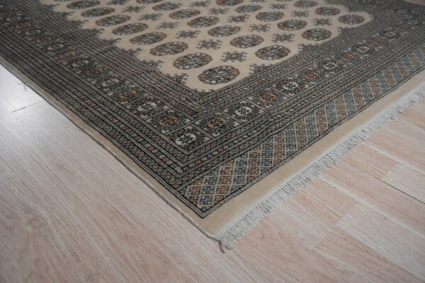 Low pile cream rug featuring geometric guls and a multi-color patterned border on light wood flooring.