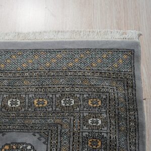 Low pile gray rug displaying detailed geometric patterns in black, gold, and mint on light hardwood floors.