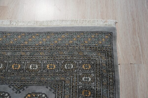 Low pile gray rug displaying detailed geometric patterns in black, gold, and mint on light hardwood floors.