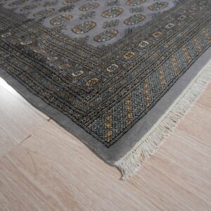 A gray rug with a yellow and teal geometric pattern and white fringe rests on light wood flooring.