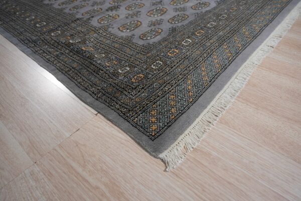 A gray rug with a yellow and teal geometric pattern and white fringe rests on light wood flooring.