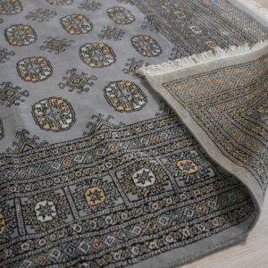 A gray patterned rug with gold and black accents lies partially folded on light wood plank flooring.