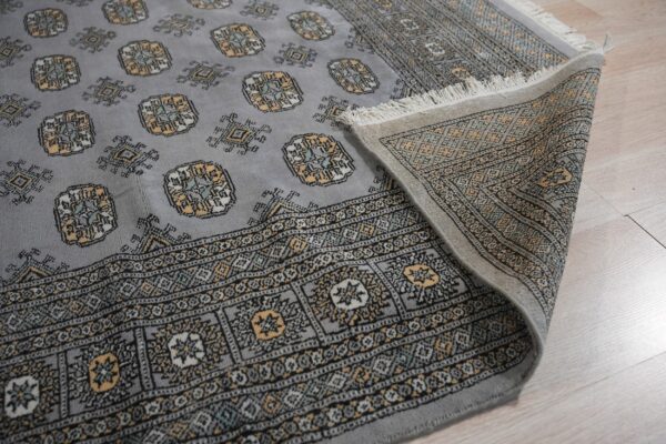 A gray patterned rug with gold and black accents lies partially folded on light wood plank flooring.