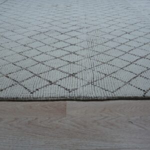 Cream textured rug with a subtle brown trellis pattern lying on light blonde hardwood flooring.