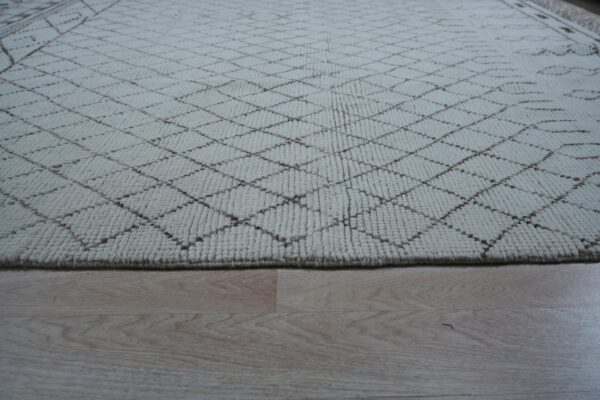 Cream textured rug with a subtle brown trellis pattern lying on light blonde hardwood flooring.