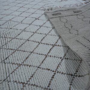 Textured off-white rug featuring a brown diamond pattern, with the woven backing visible on light wood flooring.