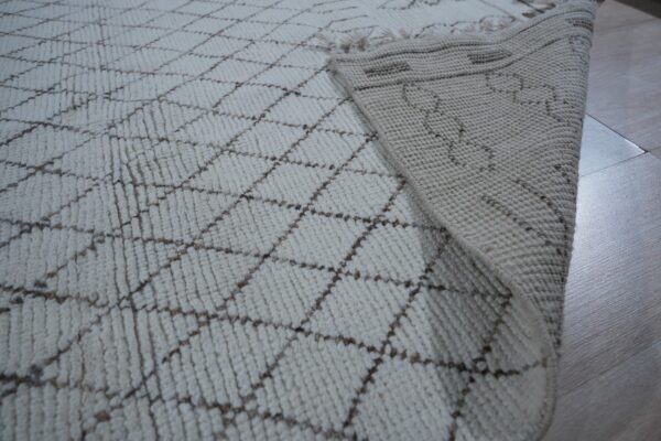 Textured off-white rug featuring a brown diamond pattern, with the woven backing visible on light wood flooring.