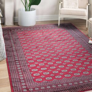Geometric red and gray patterned rug placed on wood flooring beside an armchair and potted plant.