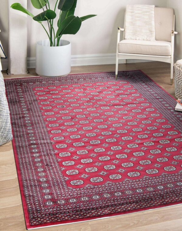 Geometric red and gray patterned rug placed on wood flooring beside an armchair and potted plant.