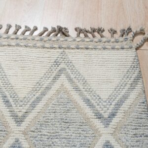 Textured cream and gray geometric pattern rug with braided tassels resting on a light wooden floor.