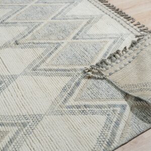 Cream and gray high-texture rug with a large diamond pattern and fringe, placed on light wood floor.