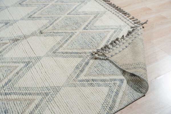 Cream and gray high-texture rug with a large diamond pattern and fringe, placed on light wood floor.