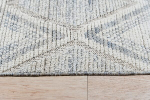 High-texture cream and gray rug with geometric pattern sits on light wood planks.