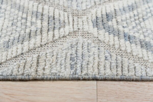 Cream and gray geometric high-low pile rug texture detail resting on light wood flooring.