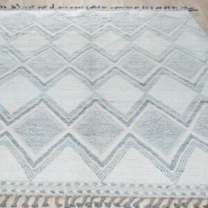 Textured off-white and gray rug with geometric diamonds and tassels rests on light wood floorboards.