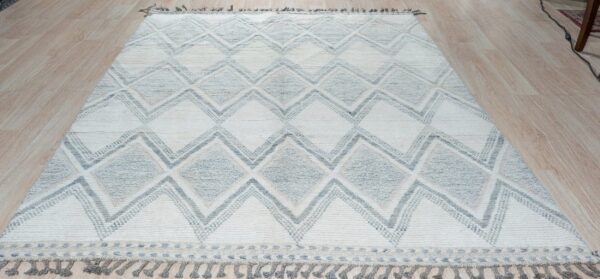 Textured off-white and gray rug with geometric diamonds and tassels rests on light wood floorboards.