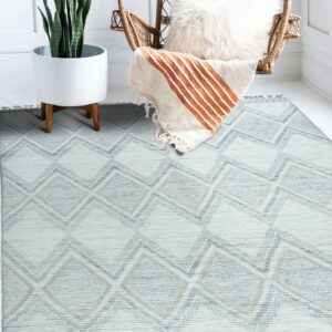 Textured cream and blue geometric rug under a wicker chair and potted plant on white floor.