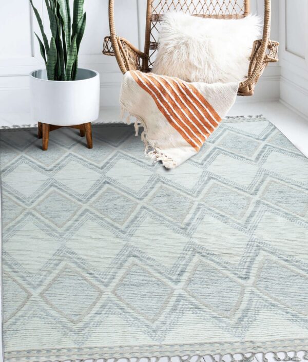 Textured cream and blue geometric rug under a wicker chair and potted plant on white floor.