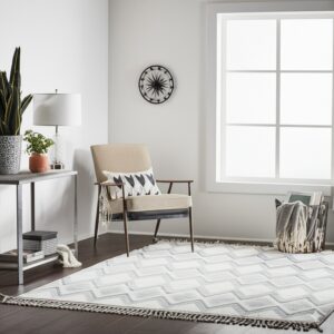 White and gray zigzag rug with fringe in a bright room featuring an armchair and dark floors.