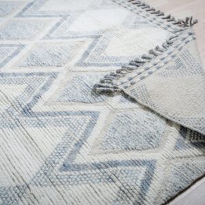 Textured off-white rug with a blue zigzag diamond pattern and tasseled edge rests on light flooring.