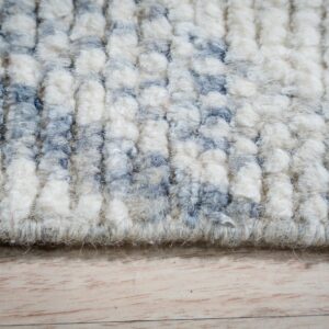 High-pile rug texture featuring thick rows of cream and dusty blue abstract patterns on light wood flooring.