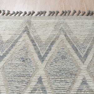 Cream and gray rug with a textured geometric pattern and fringe resting on wood flooring.