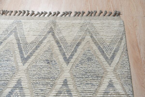 Cream and gray rug with a textured geometric pattern and fringe resting on wood flooring.