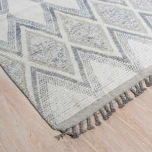 Thick pile rug with gray geometric diamonds on a cream background and gray tassels, resting on light wood flooring.